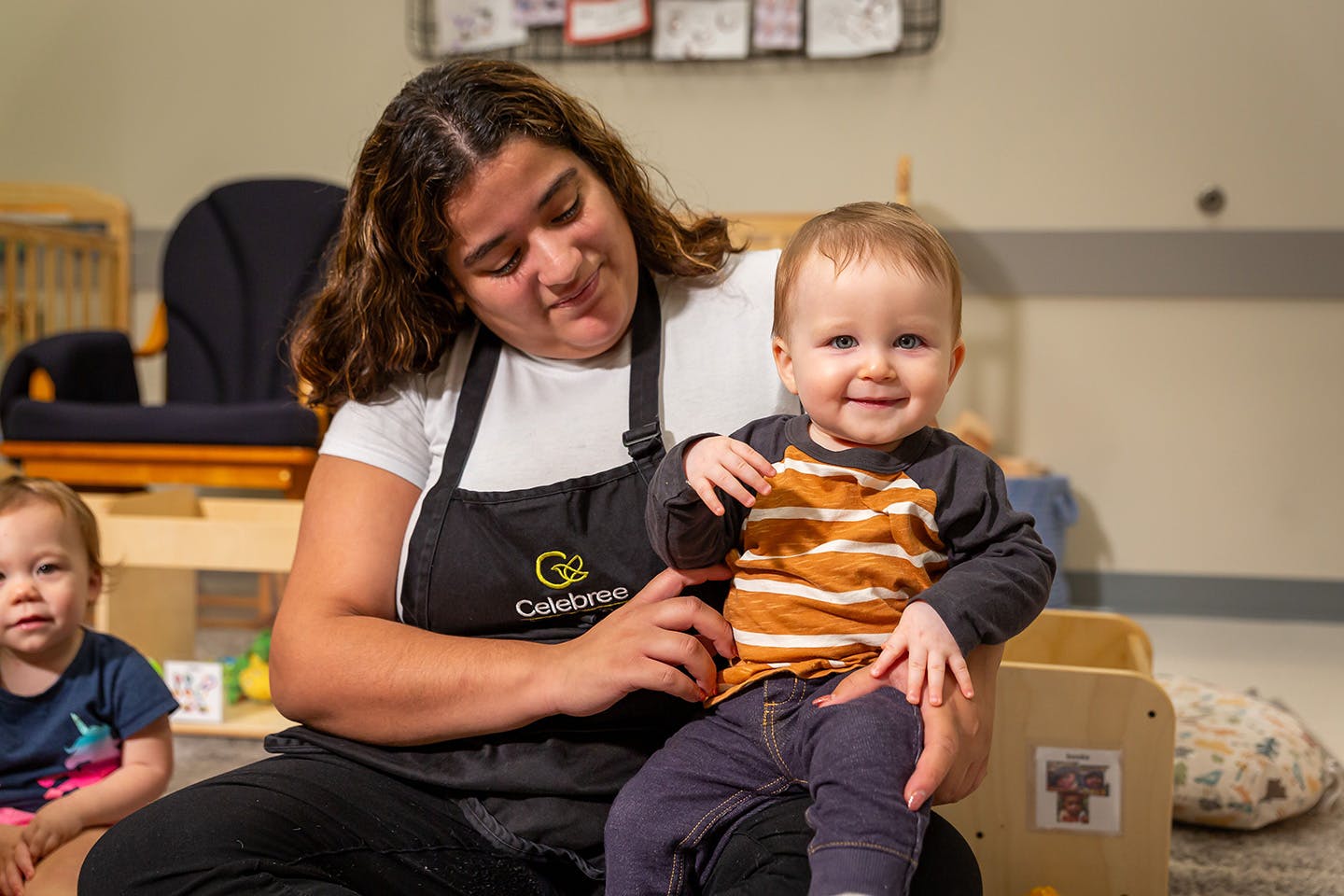 Person in apron holding a child, another child nearby