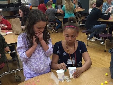 Two children at a table, one mixing something in cups