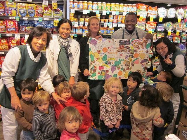 Adults and children holding a large colorful drawing in a store aisle with shelves of products