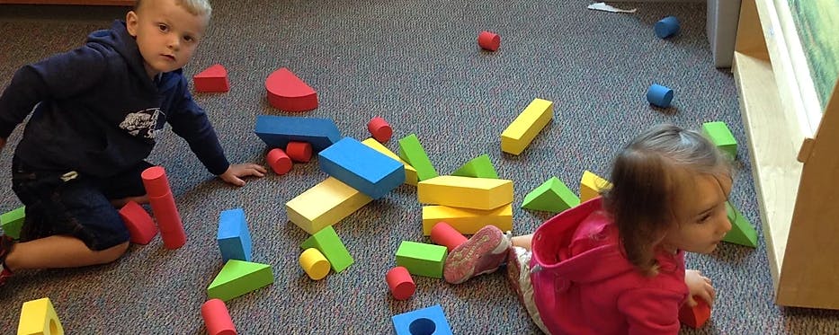 Two children playing with colorful blocks on a carpeted floor