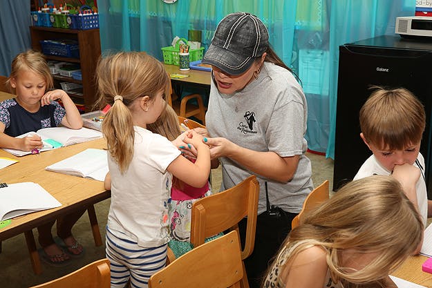 Adult helping a child in a classroom with other children at desks