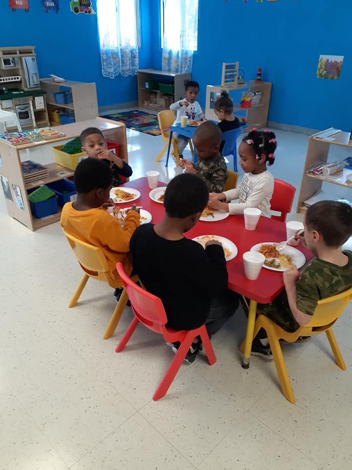 Children eating at a red table in a classroom