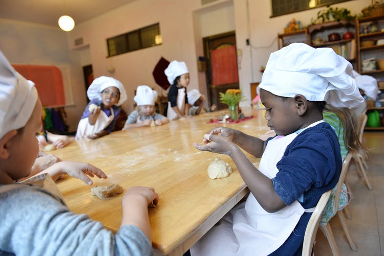 Children in chef hats and aprons making dough at a table