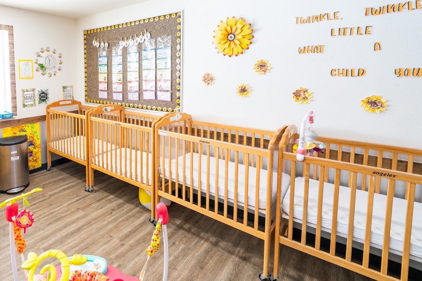 Wooden cribs lined up in a childcare classroom with decorative wall art