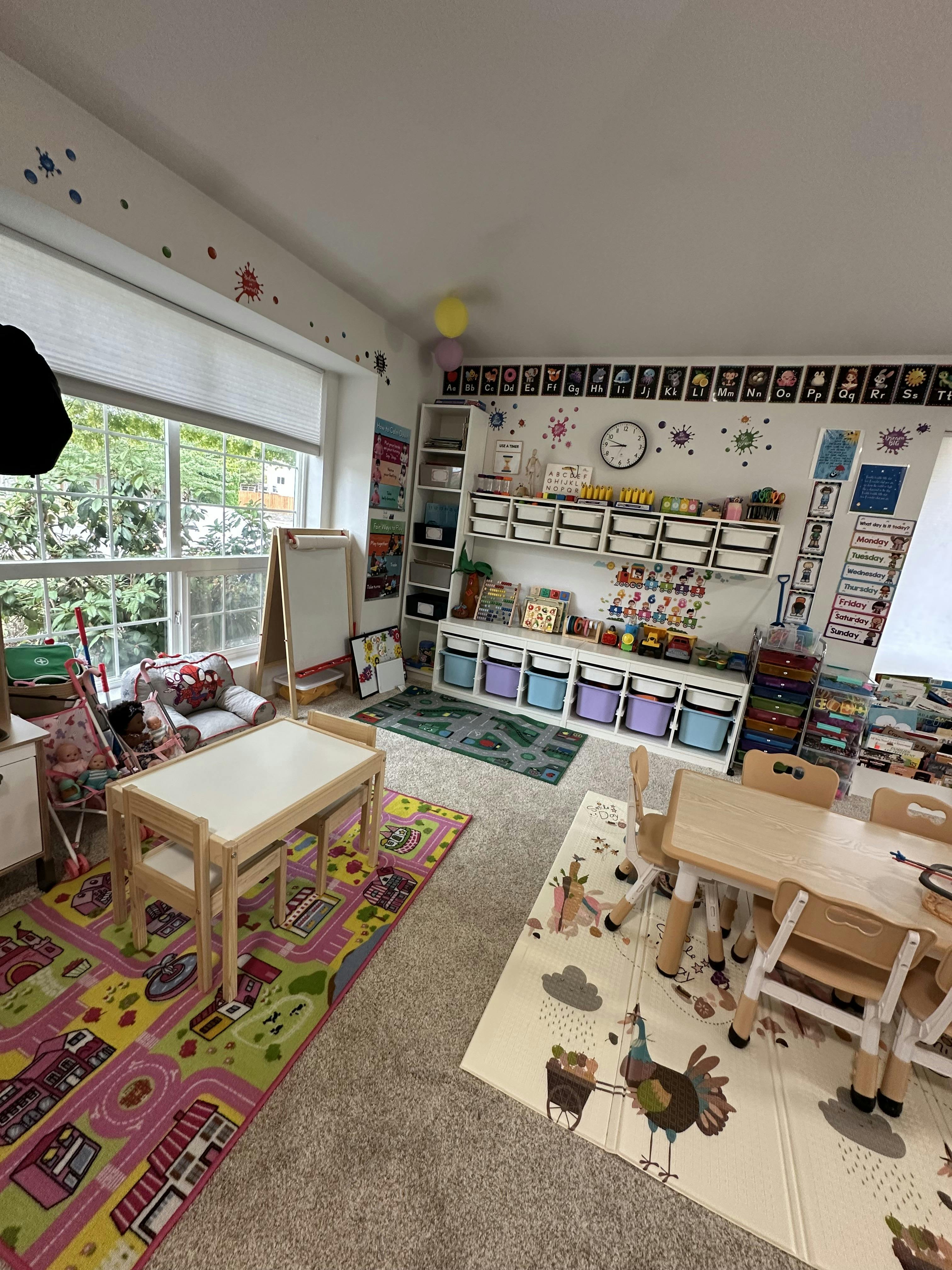 Playroom with small tables, chairs, colorful rugs, and toy storage shelves