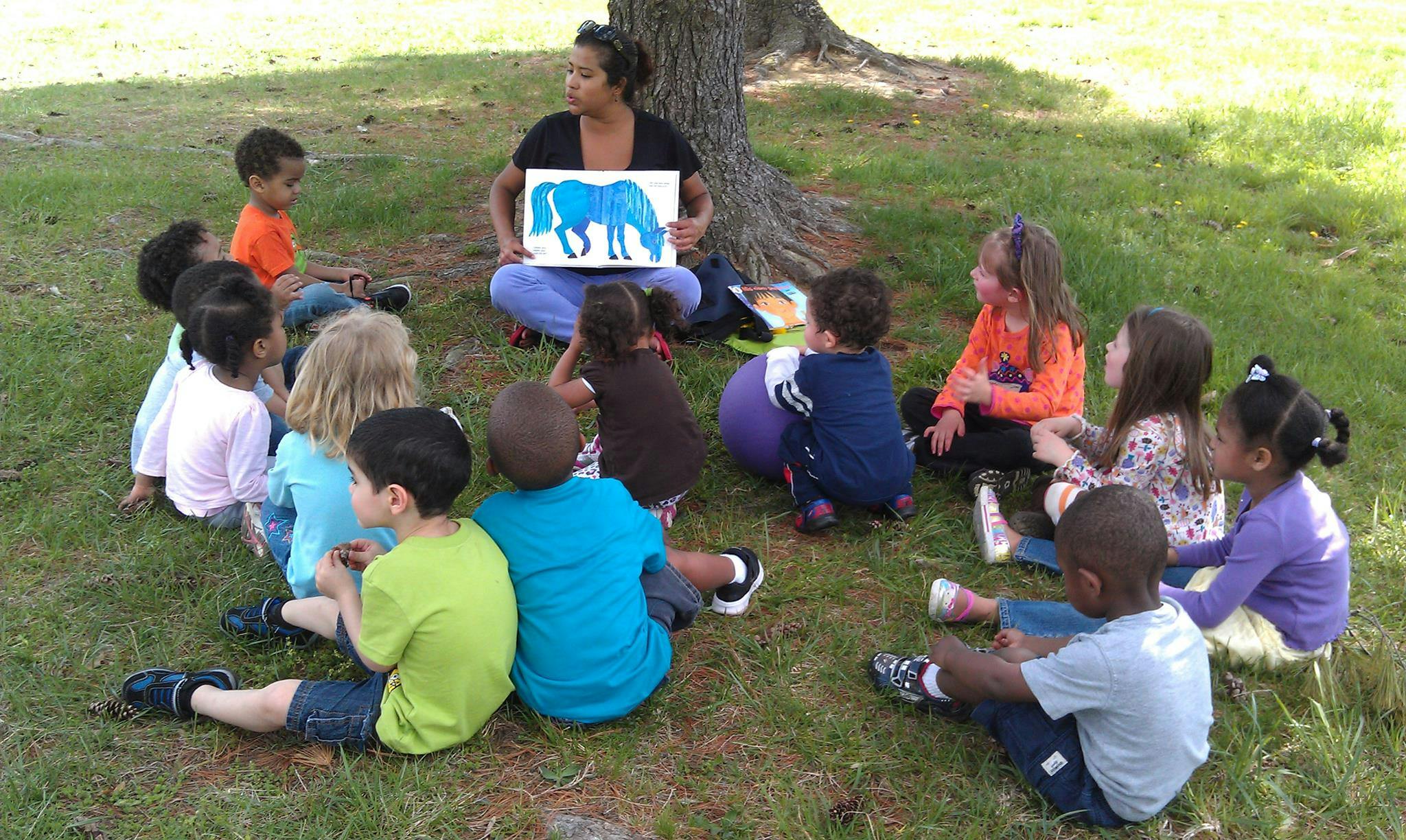 Person holding up a drawing of a blue horse to a group of children
