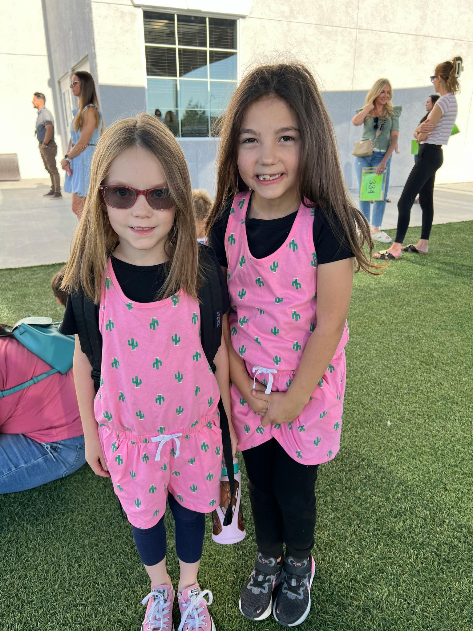 Two children standing on grass, one wearing sunglasses