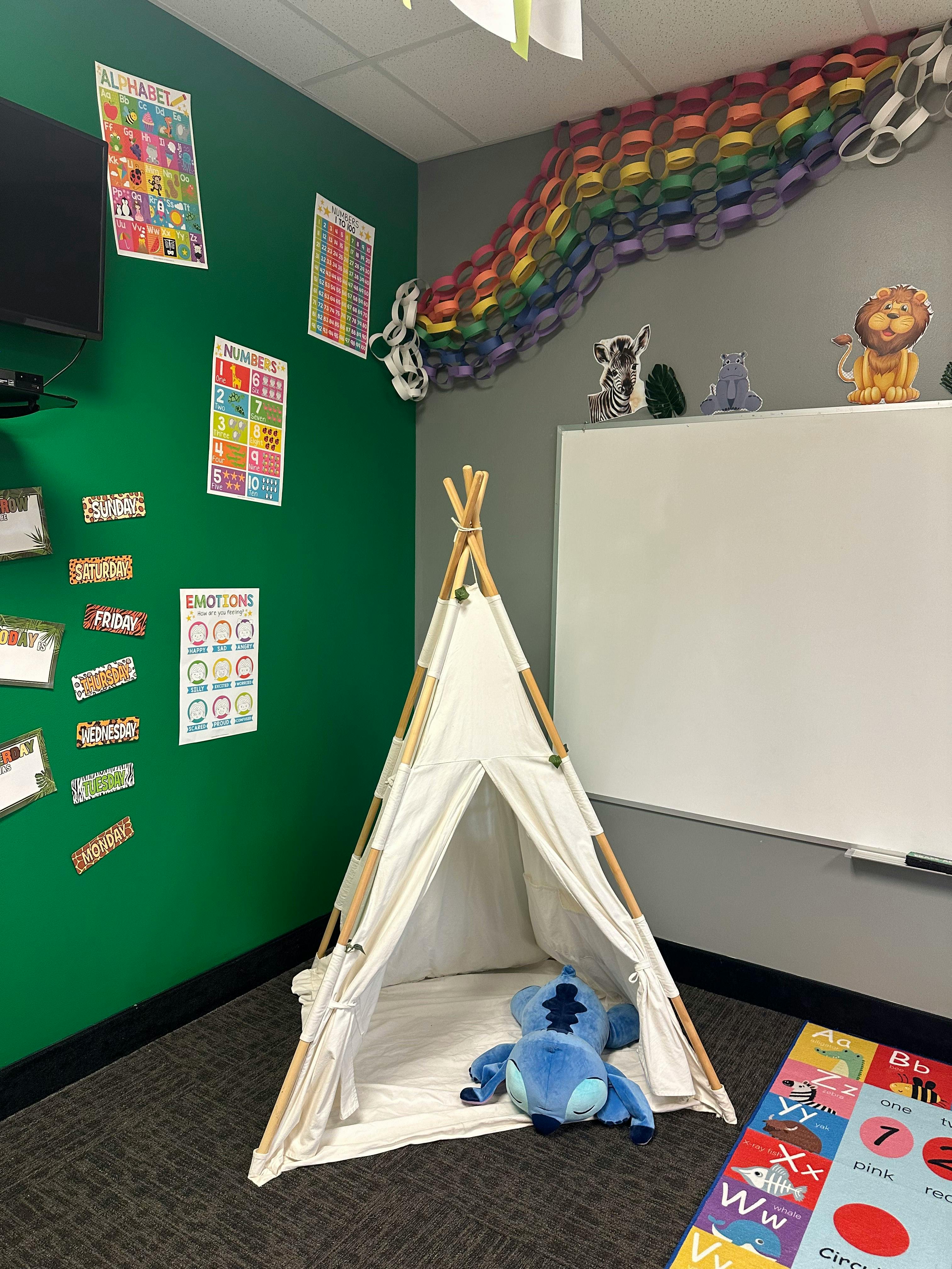 White teepee with a blue stuffed animal inside, next to a whiteboard