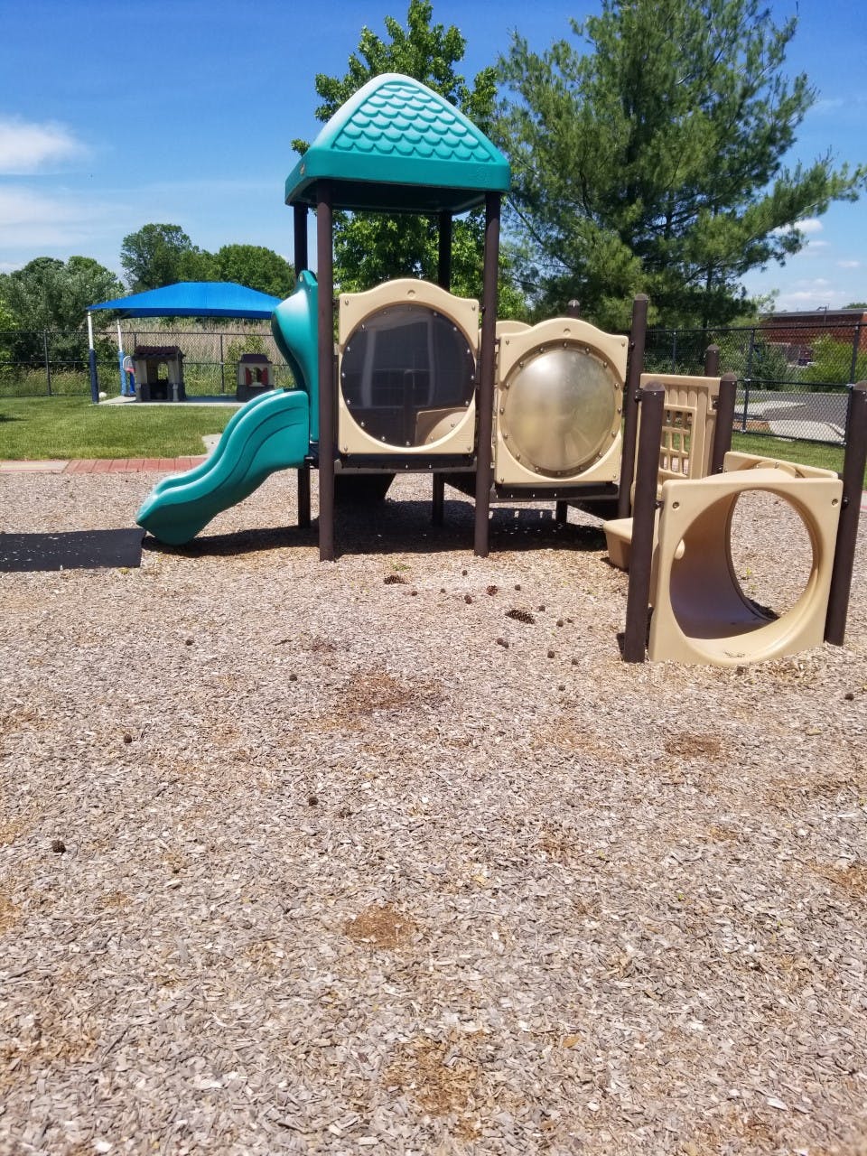 Empty playground with a teal and tan play structure, slide, and tunnel