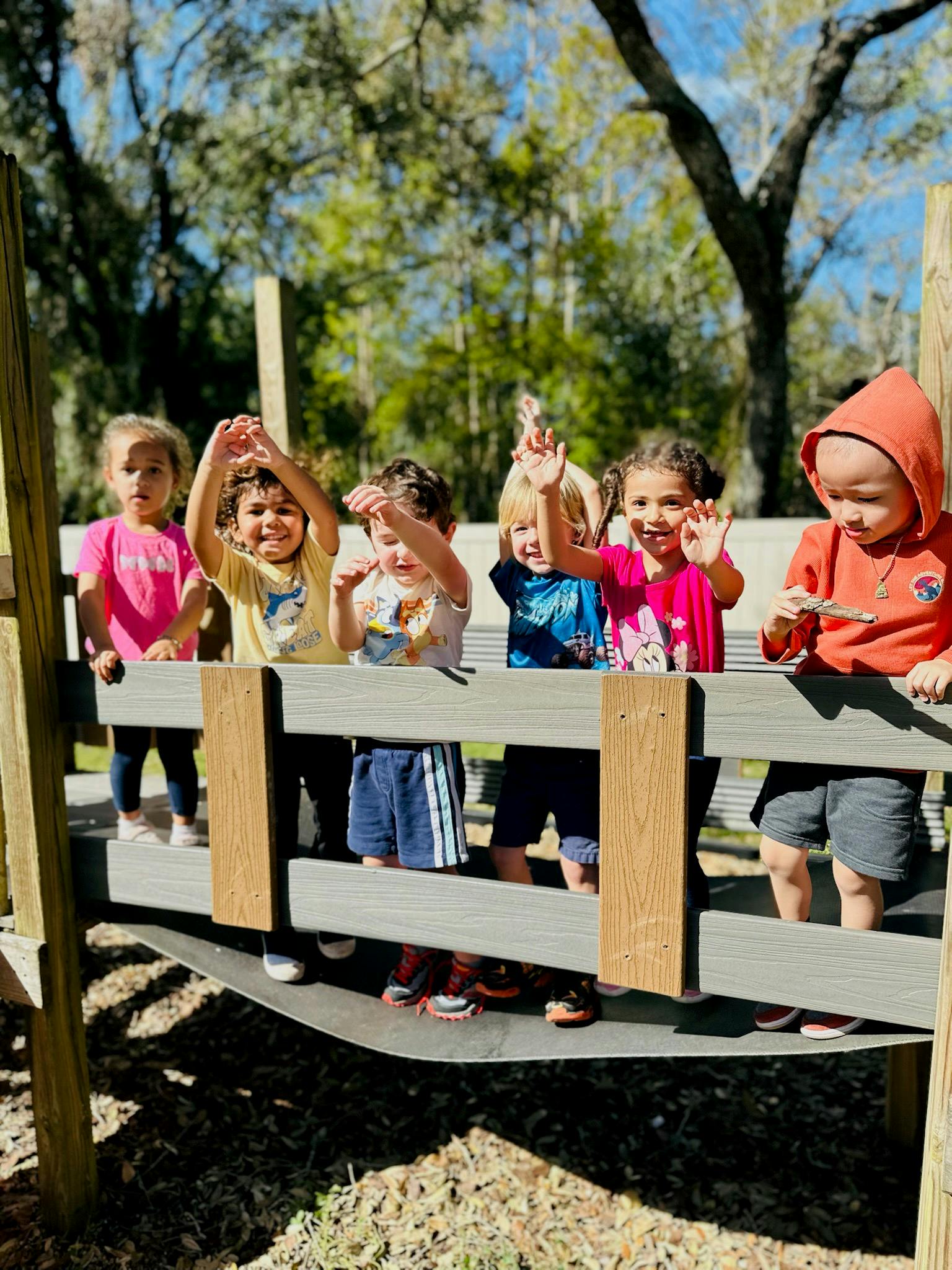 Group of children on a playground structure, some waving