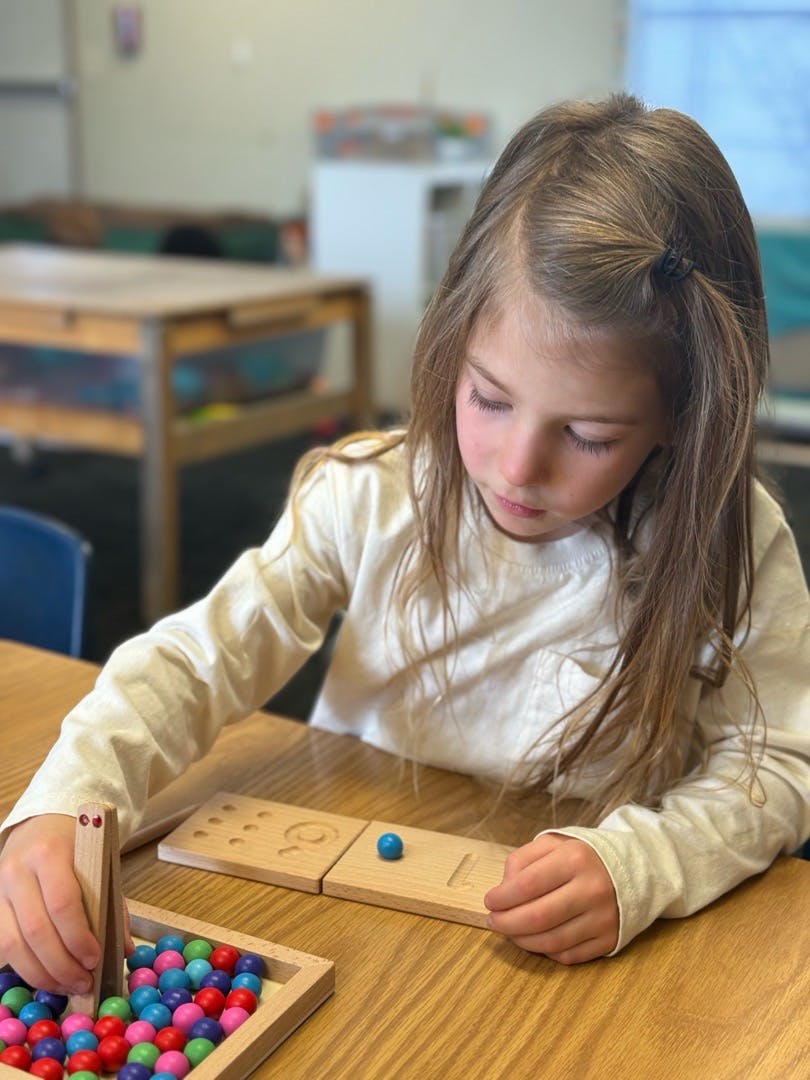 Child playing with colorful beads and wooden learning tools at a table
