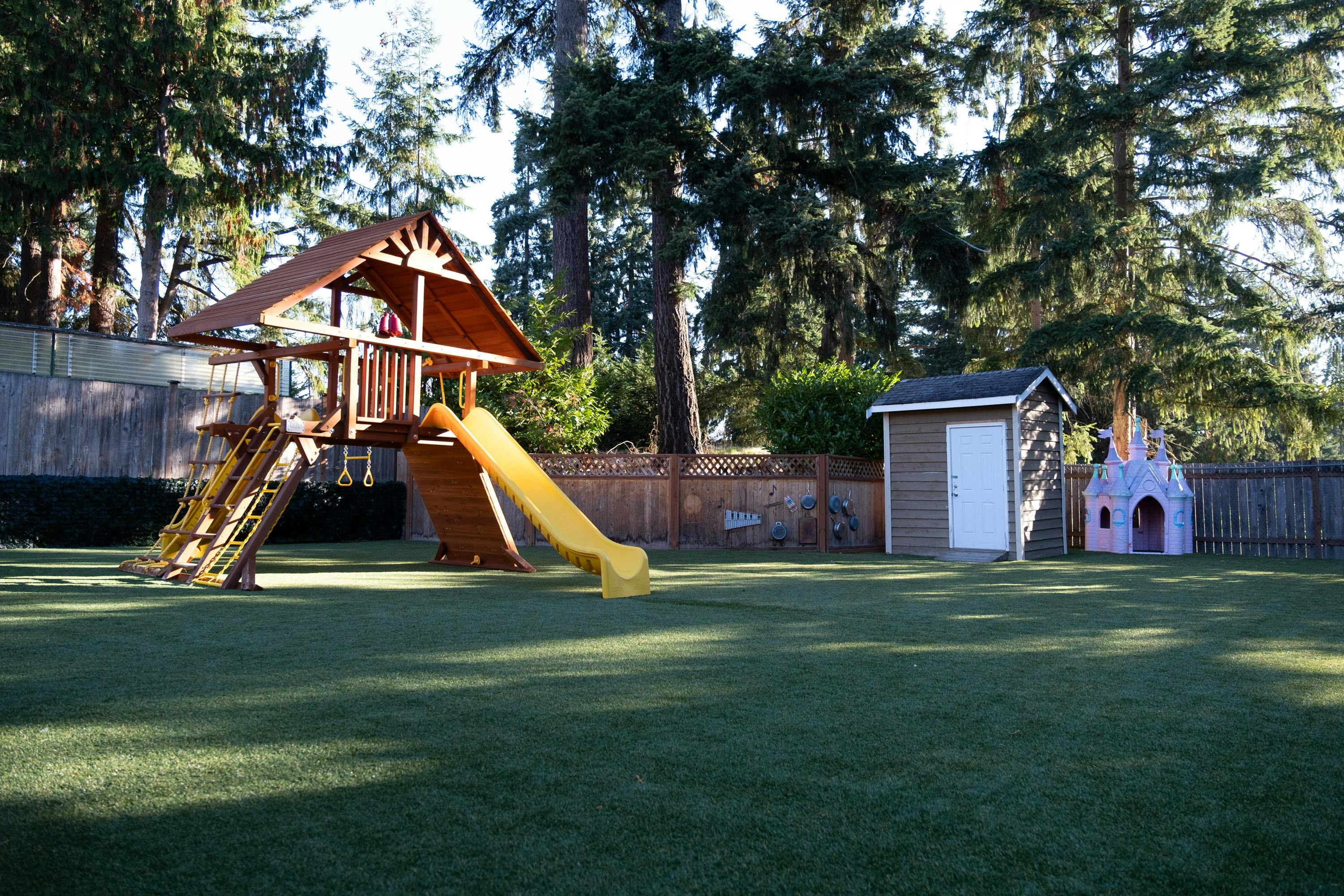 Wooden playground structure with a yellow slide on artificial turf