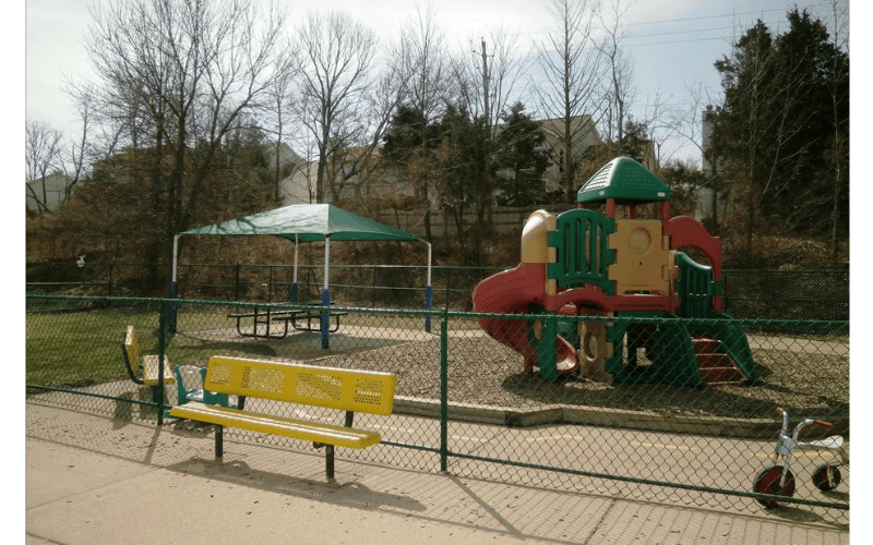 A fenced-in playground with a slide structure and covered picnic table