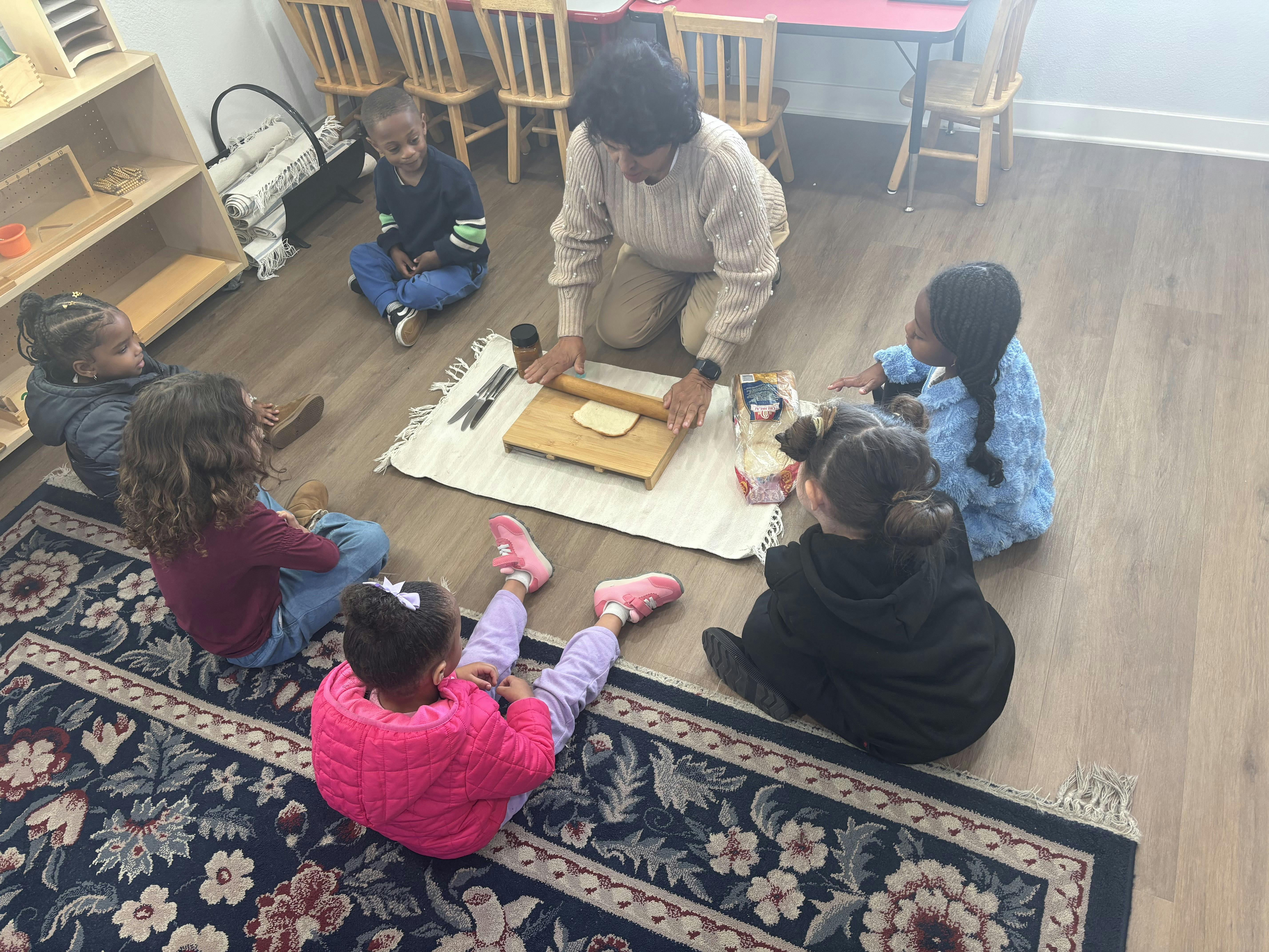 An adult and several children sitting on the floor making bread with a rolling pin