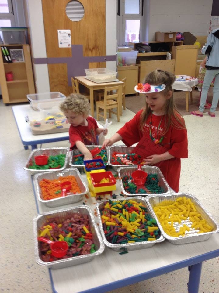 Two children playing with colorful pasta and other sensory bin materials