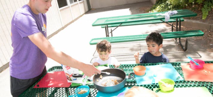 Person serving food to two children at a picnic table