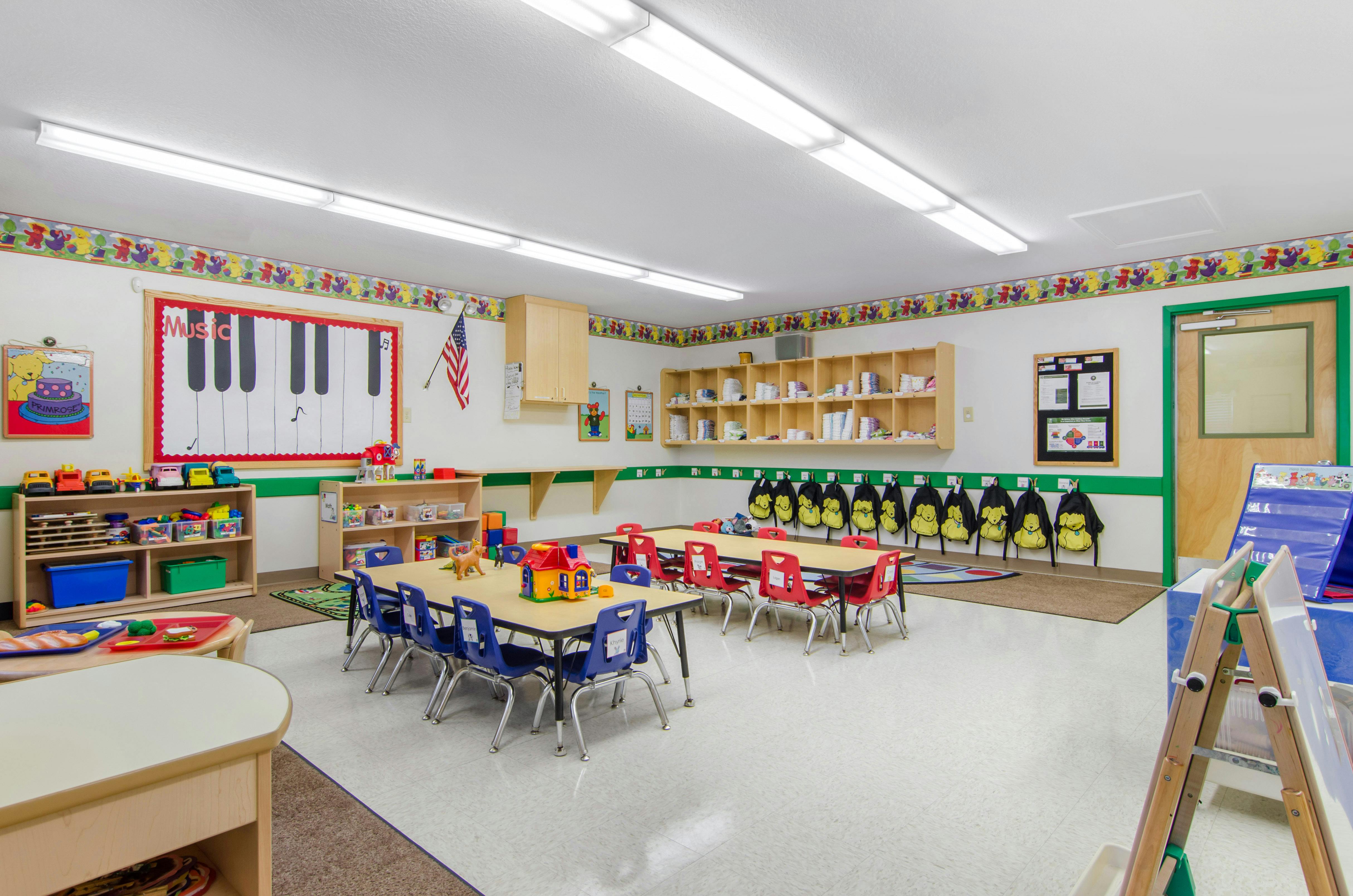 Classroom with child-sized tables and chairs, shelves of toys, and a piano-themed bulletin board