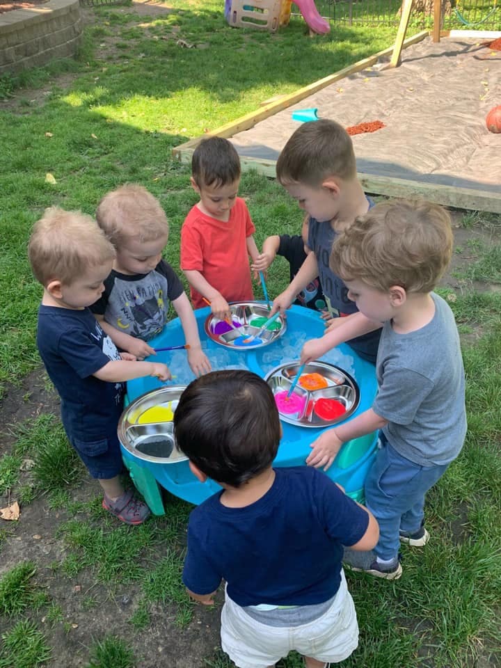 Children gathered around a table with paint and brushes
