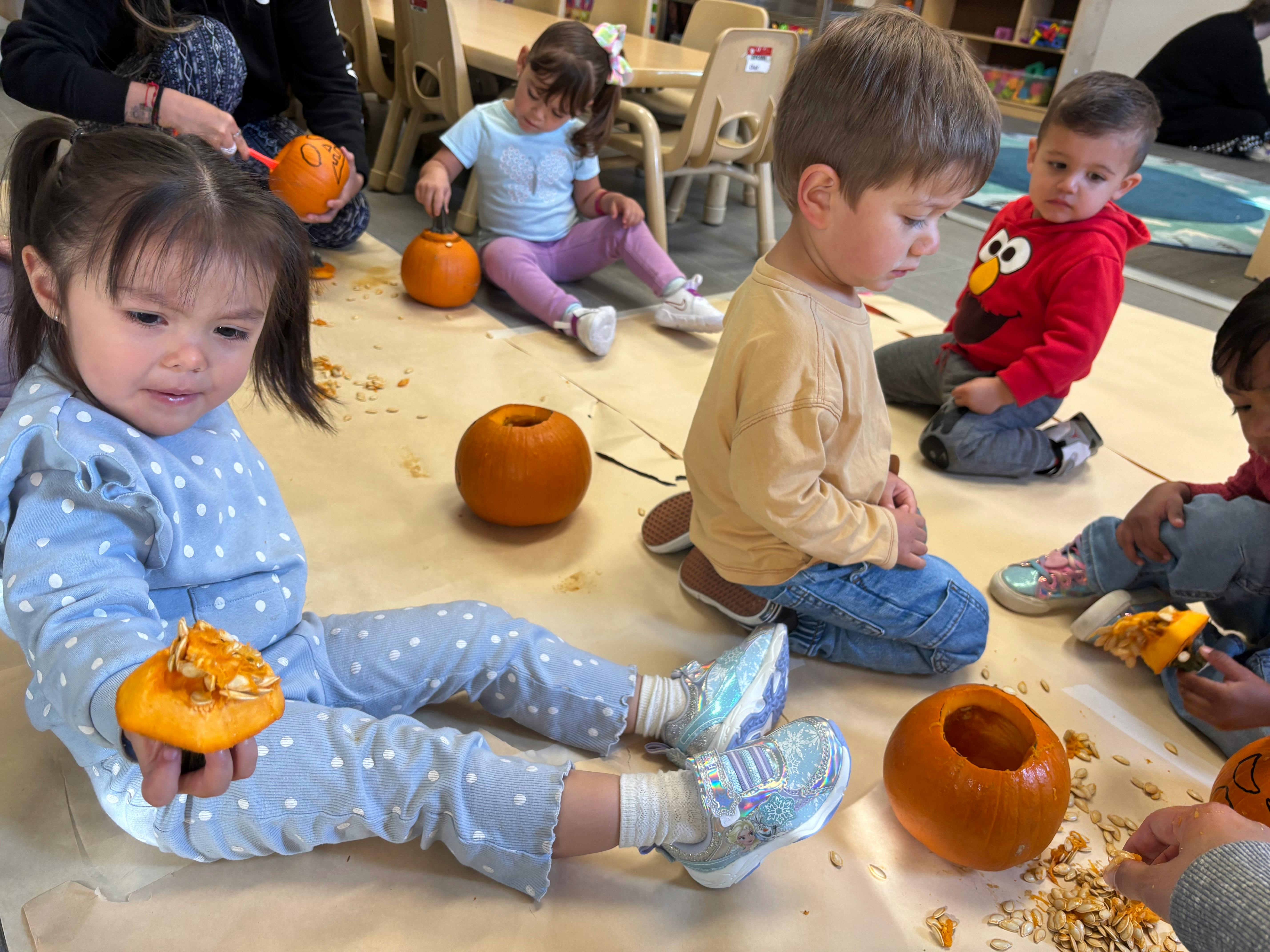 Children sitting on the floor with pumpkins and pumpkin seeds