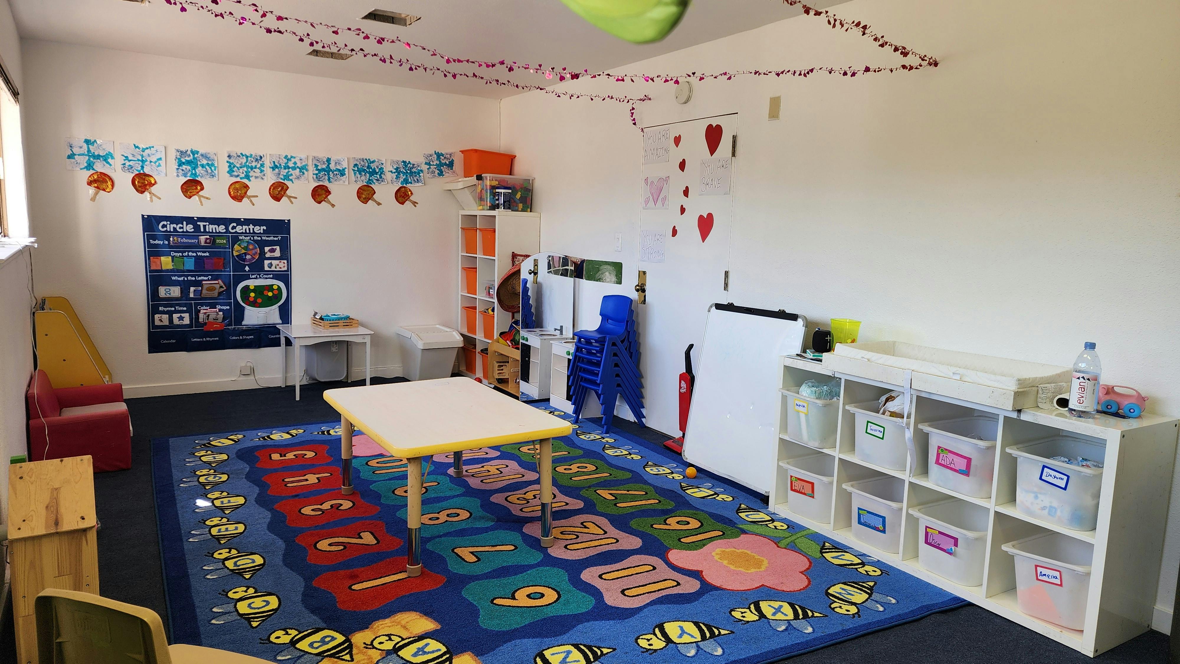 Classroom interior with a colorful number rug, small tables, and toy storage bins