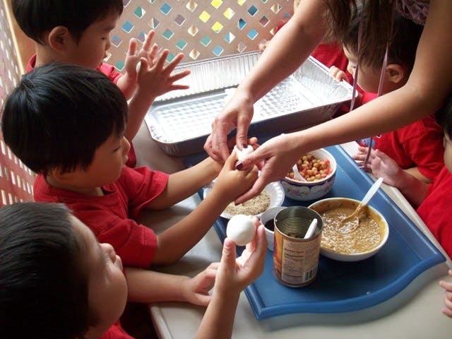 Adult helping children peel eggs at a table