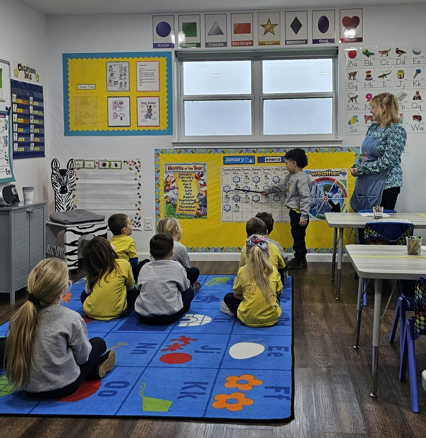Adult and children in a classroom, child pointing at a board