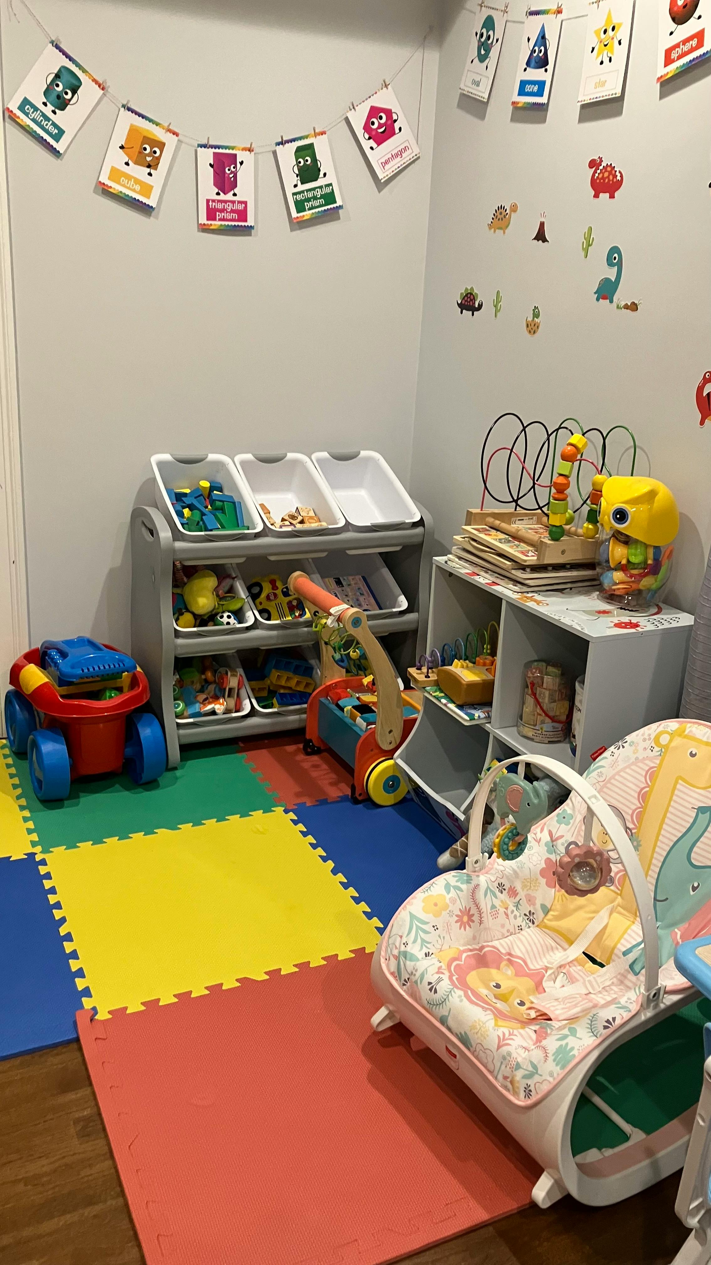 Playroom with toy storage, colorful floor mats, and baby bouncer