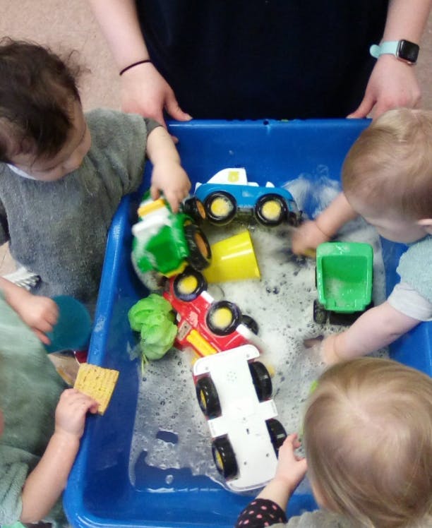 Children playing with toy cars in a blue bin with soapy water