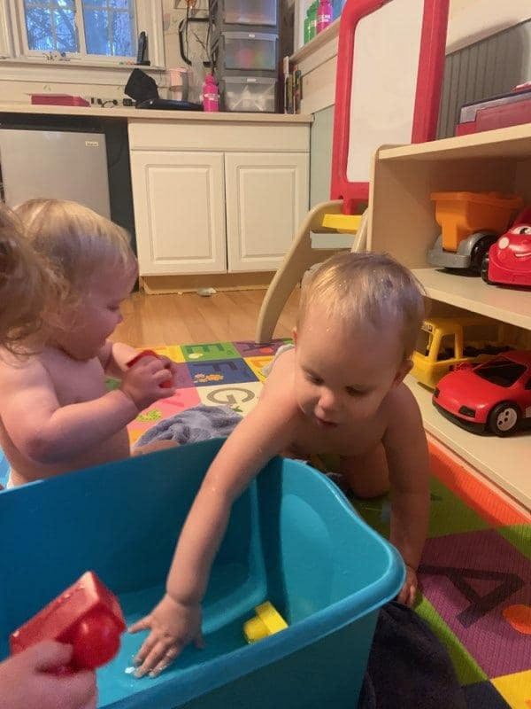 Two children playing with toys in a blue bin