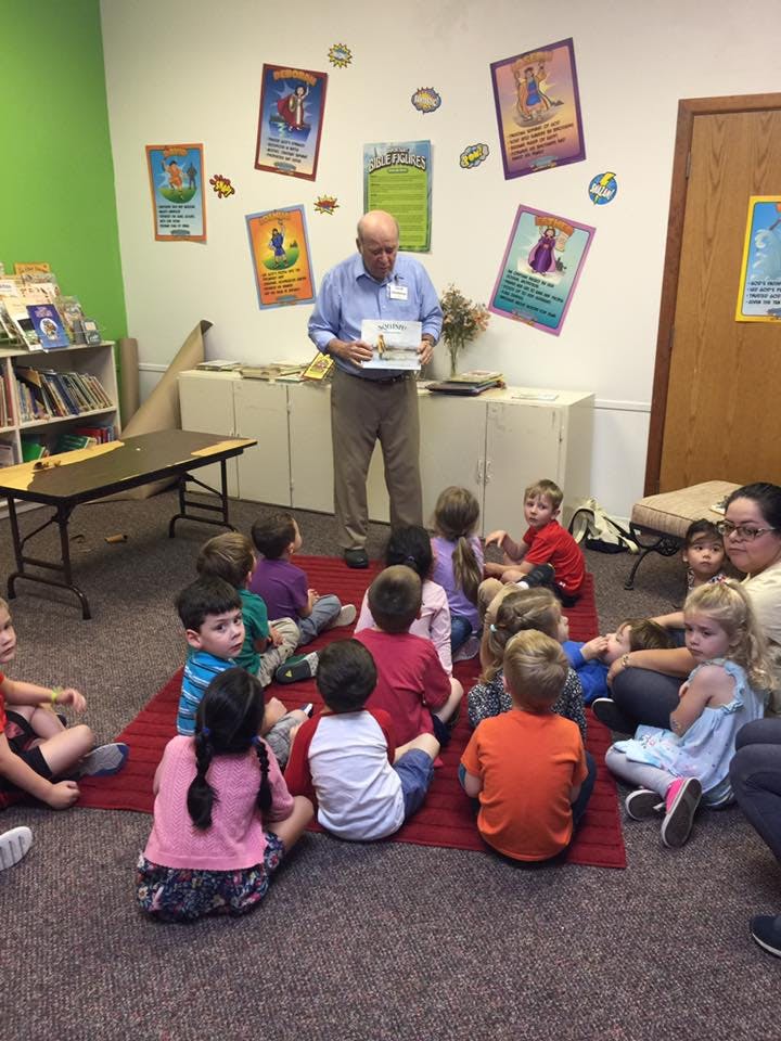 Adult person reading a book to a group of children sitting on a rug