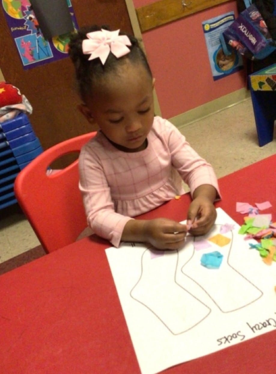Child decorating paper sock cutouts with small colorful pieces