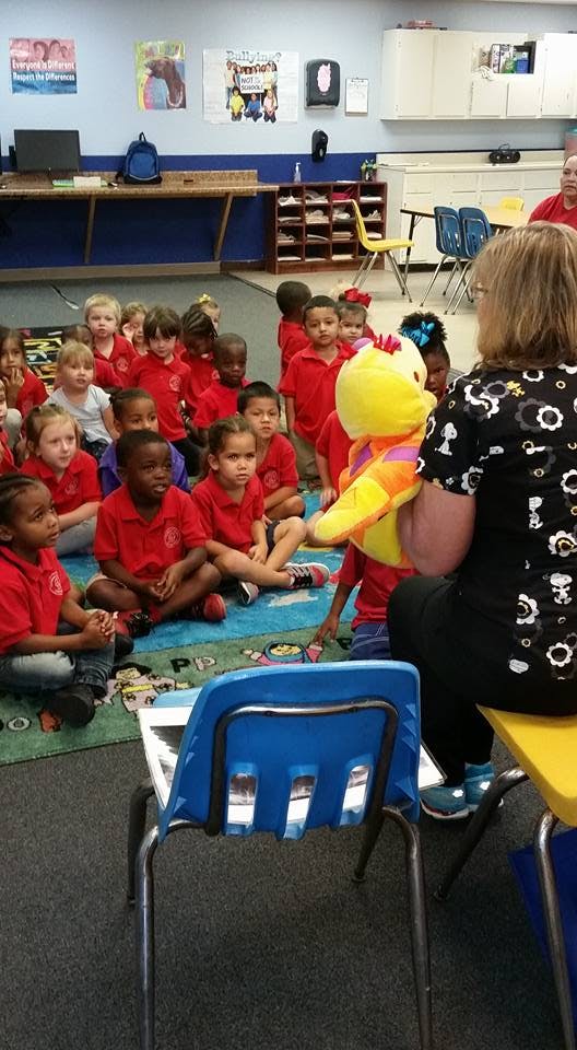 Adult holding a puppet for children sitting on a rug in a classroom