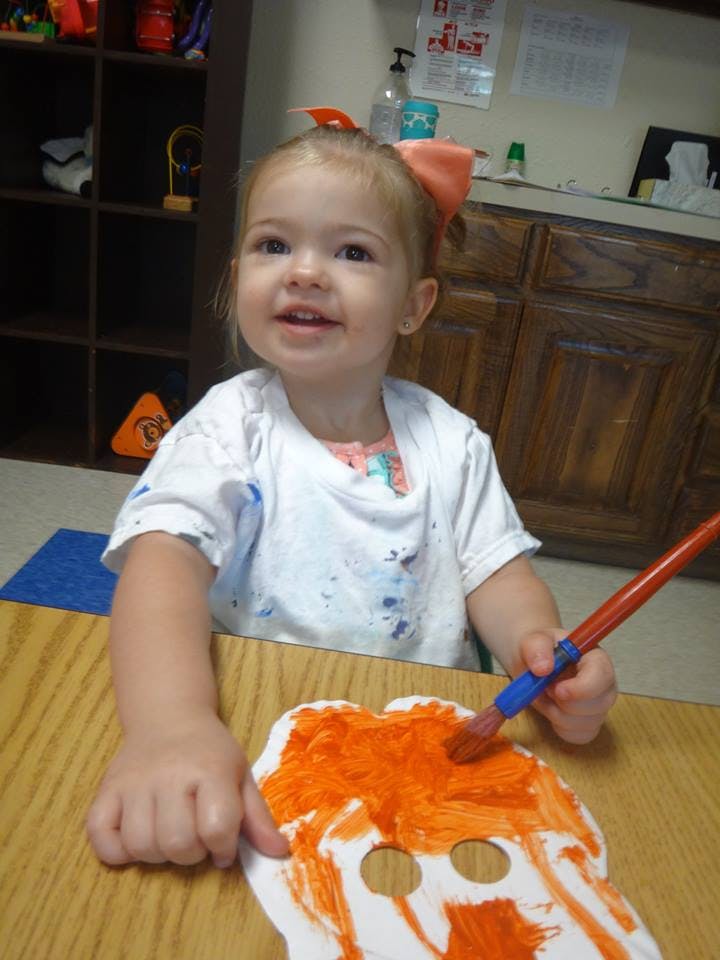Child painting a paper mask orange
