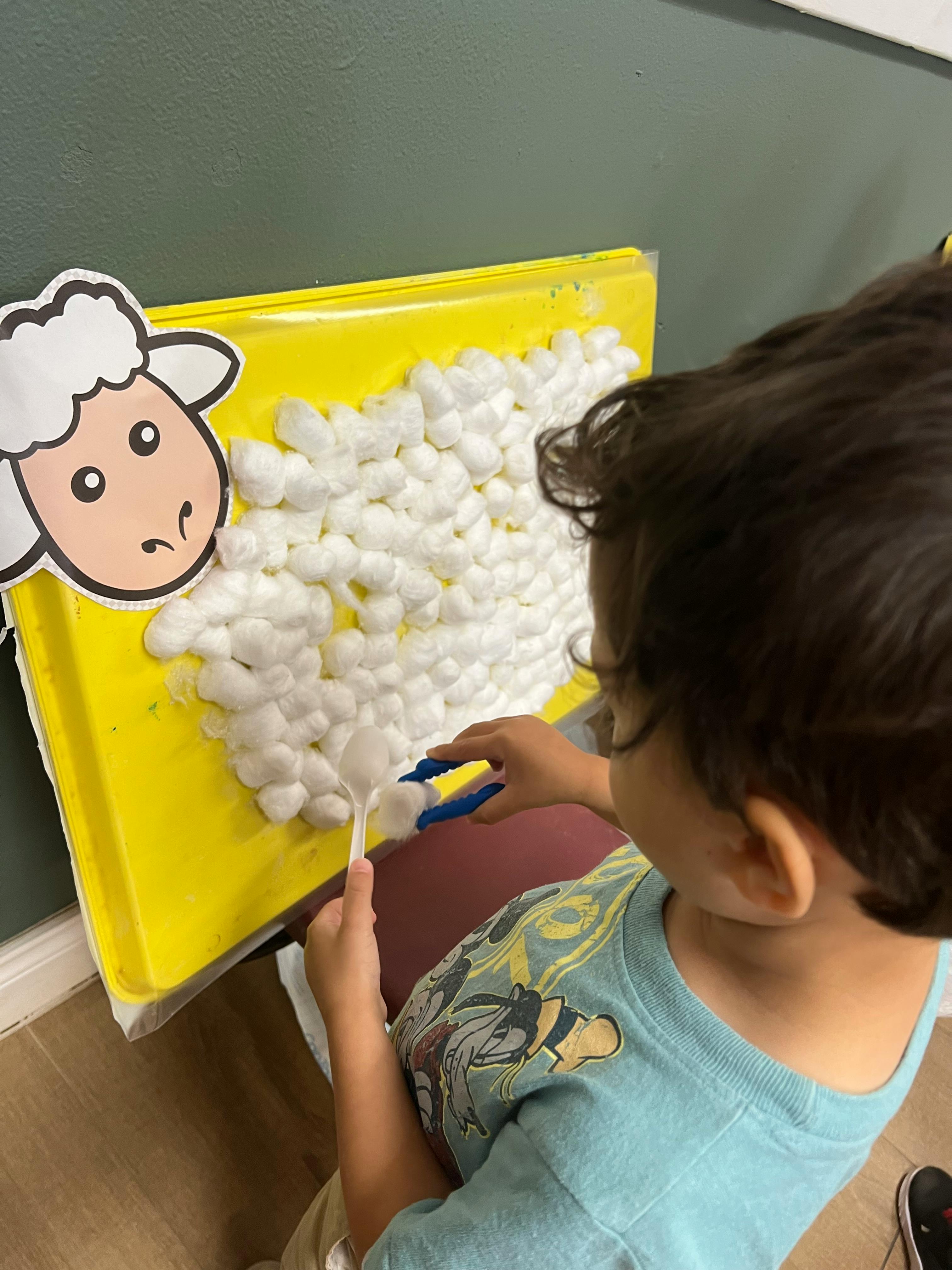 Child using tongs to place cotton balls on a sheep craft