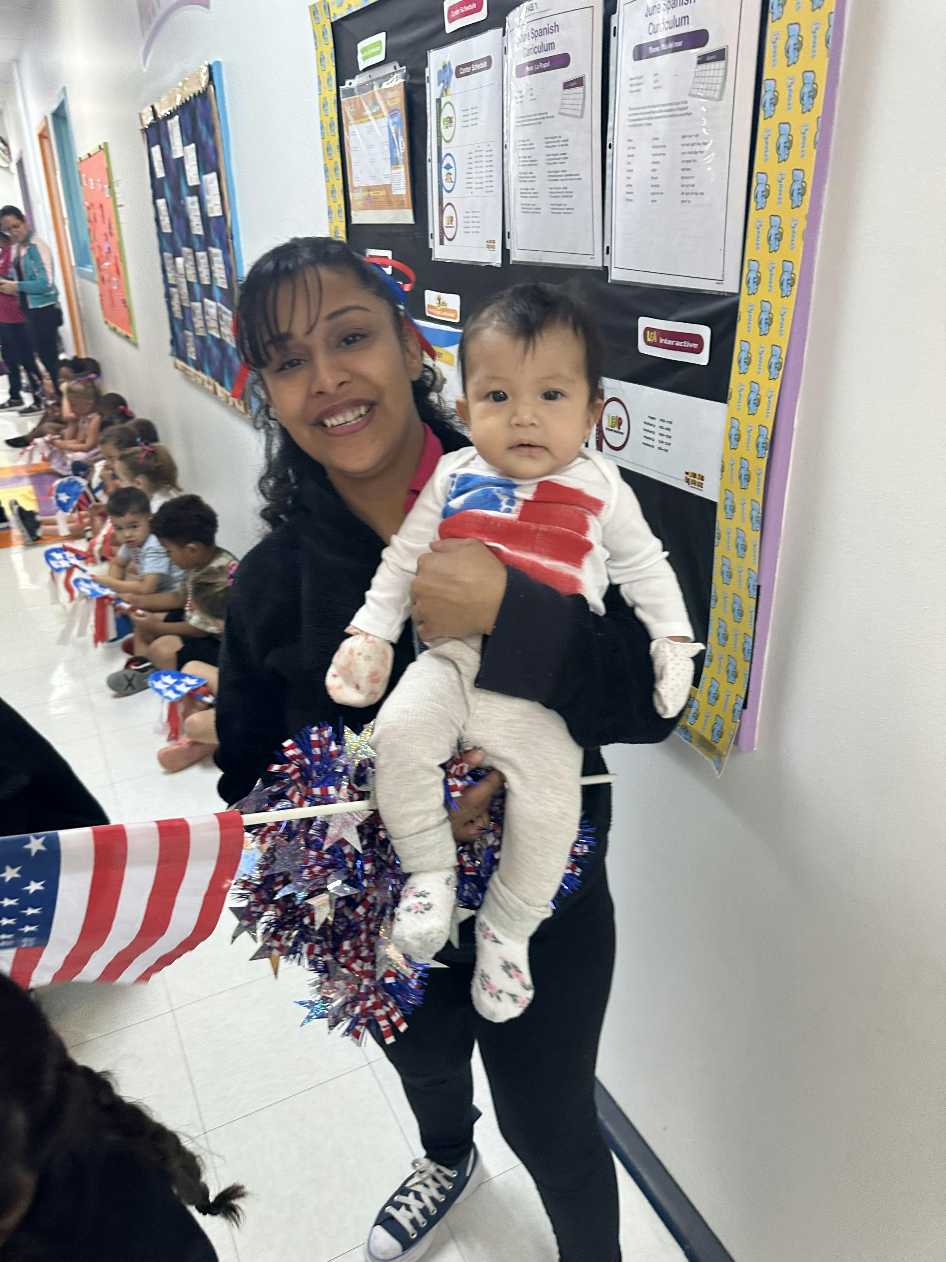 Person holding a child in a classroom with other children sitting on the floor