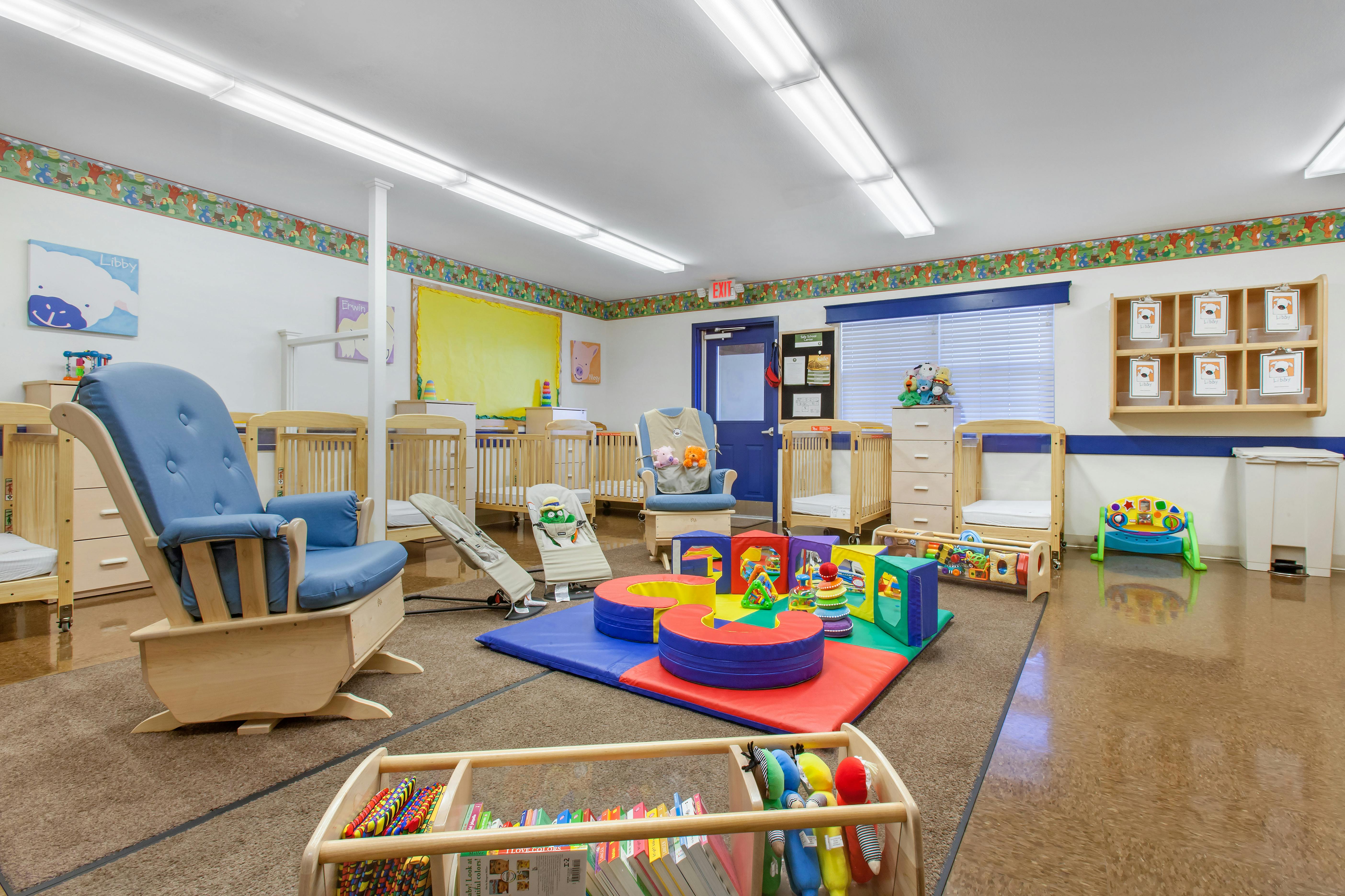 A colorful childcare room with cribs, two rocking chairs, and play mats with toys