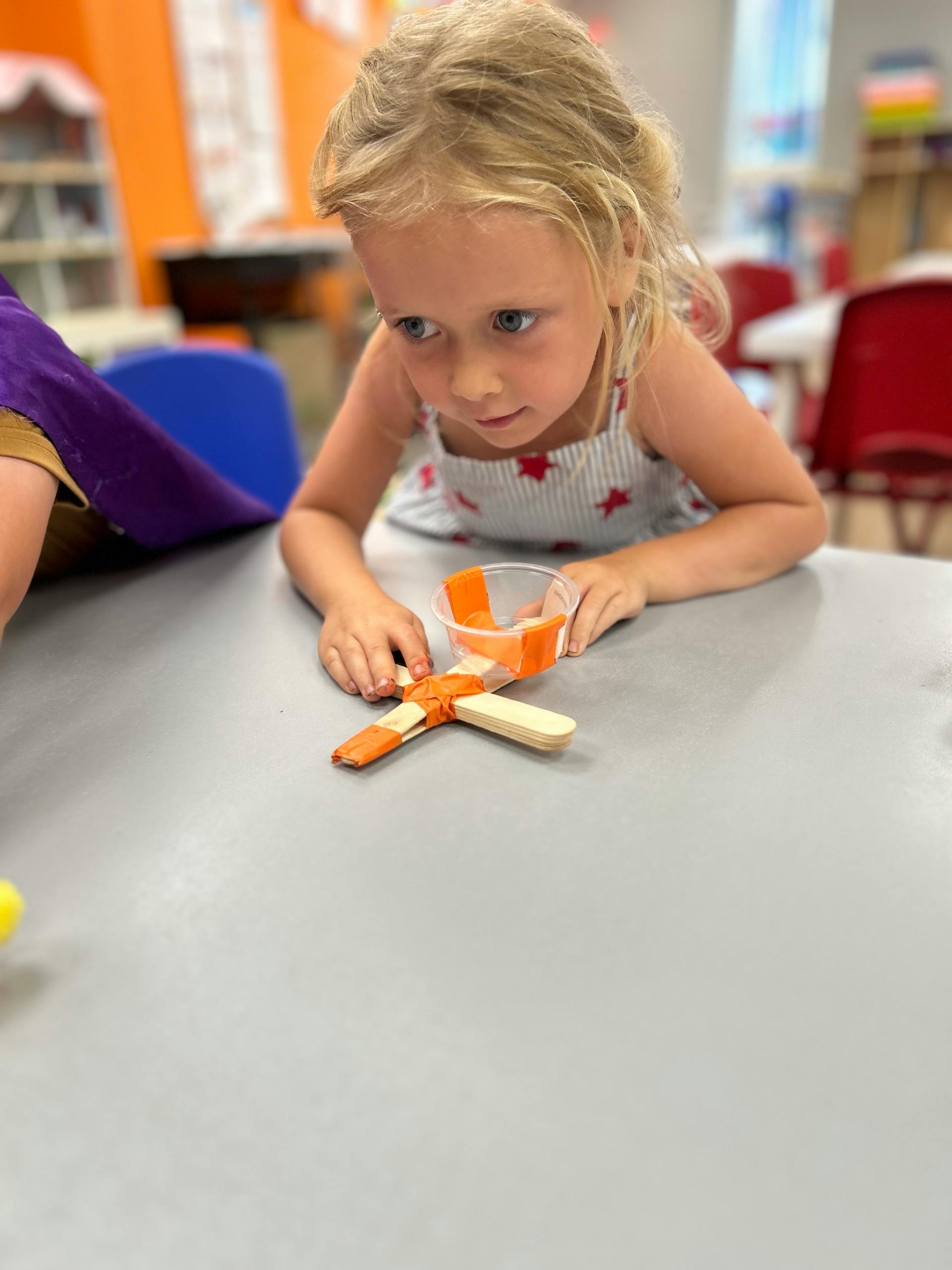 Child building a catapult with craft sticks and tape in a classroom
