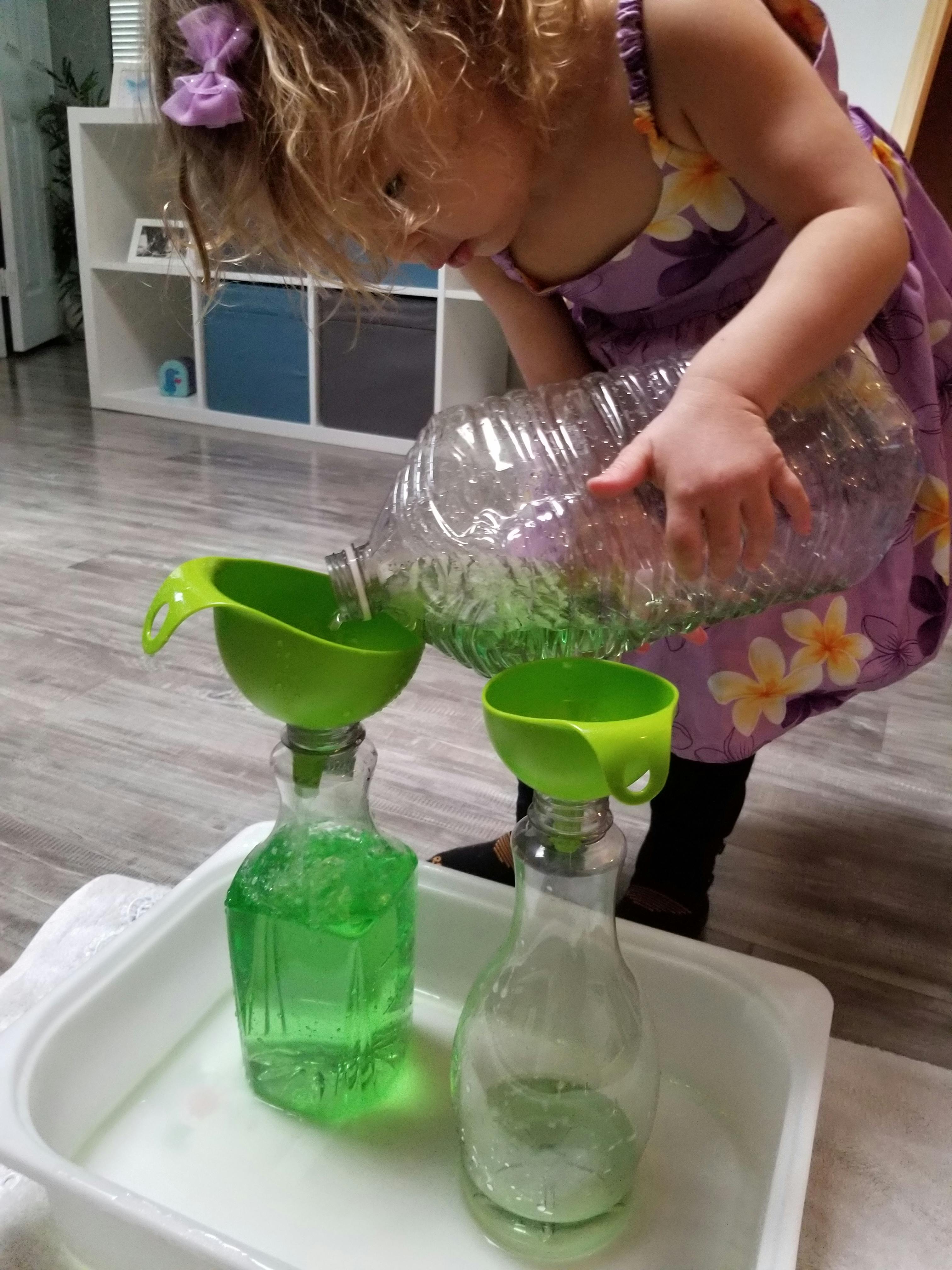 Child pouring liquid from a large bottle into a smaller bottle through a funnel
