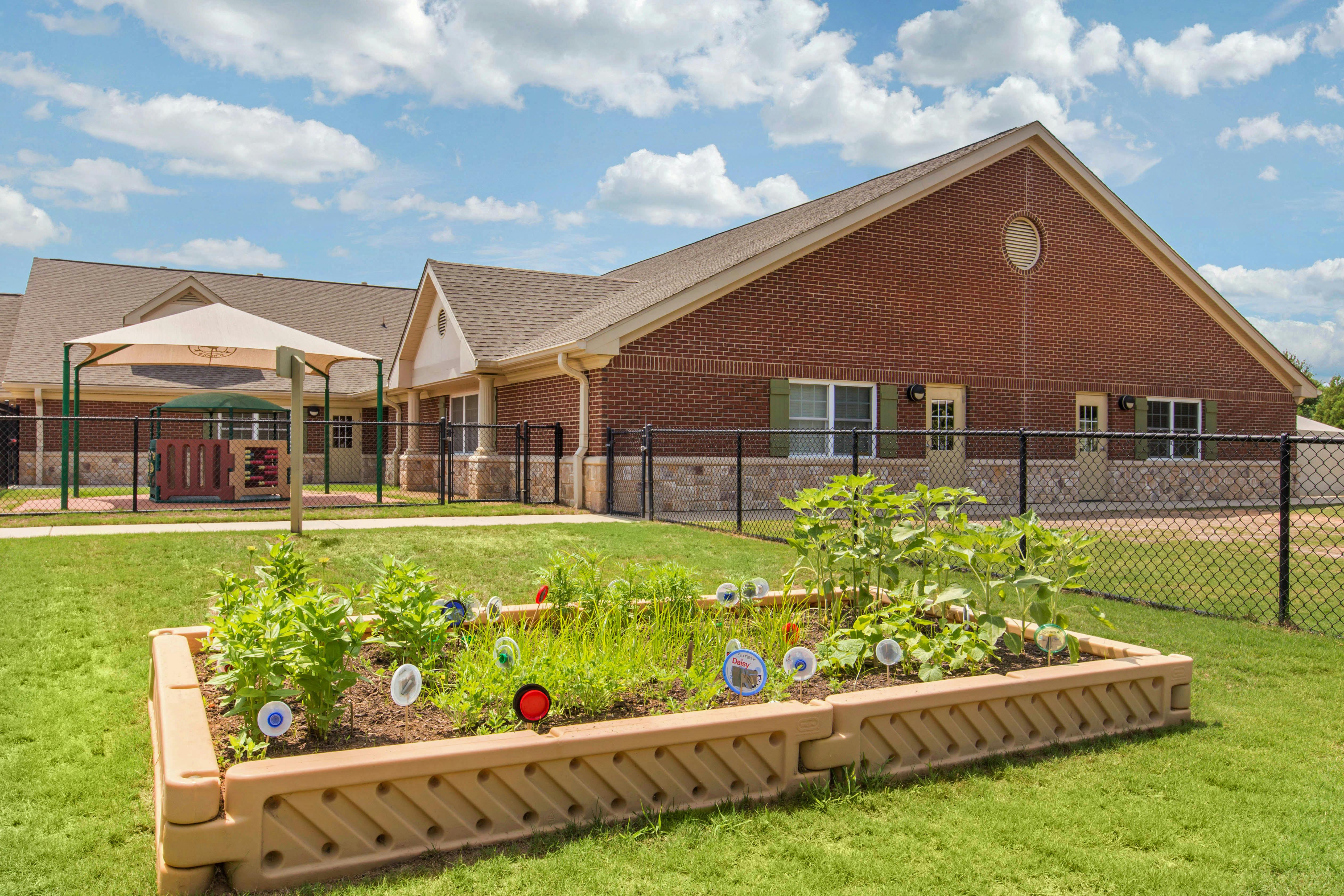 Raised garden bed with young plants and garden markers in front of a building