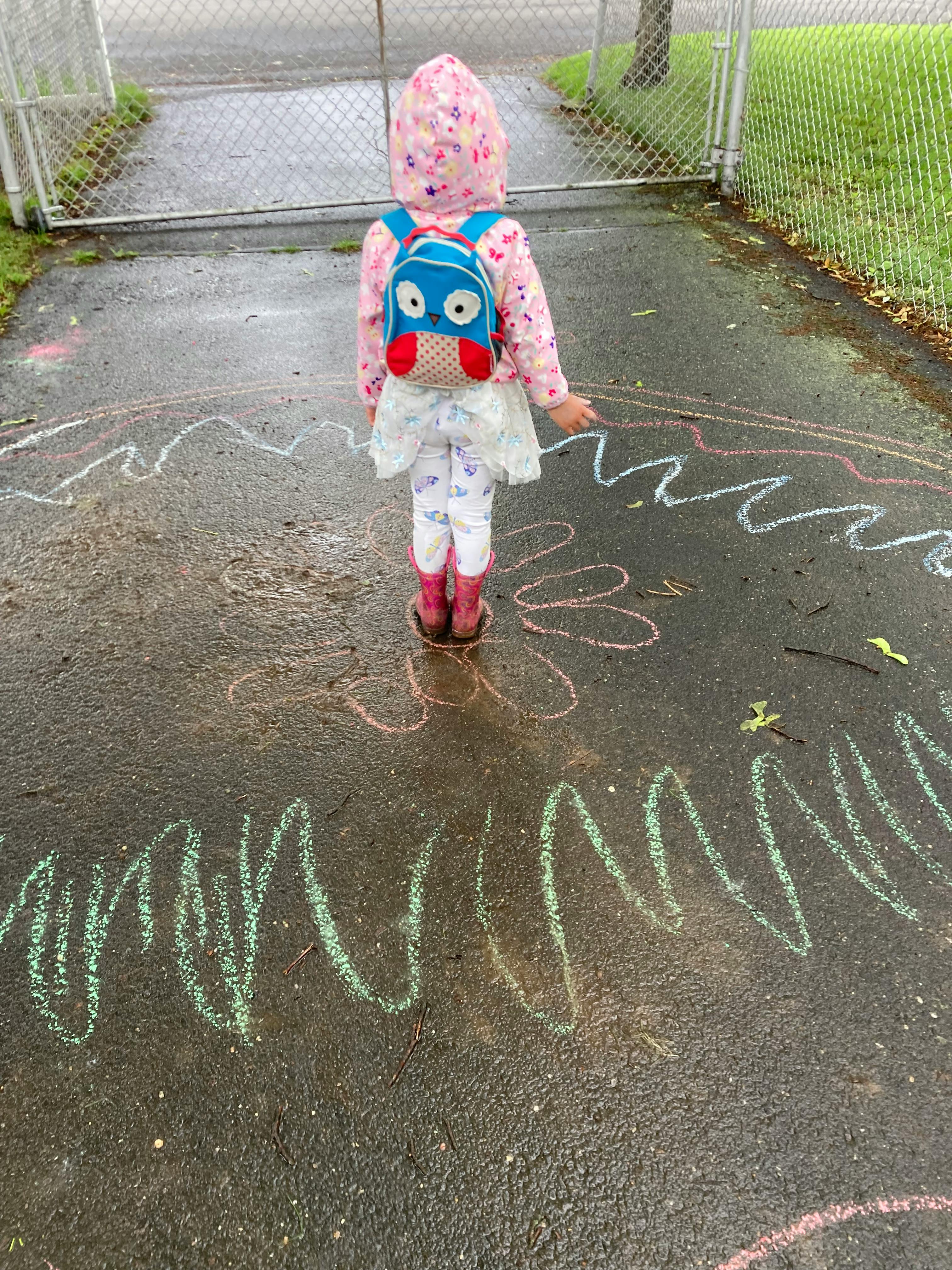 Child in a hooded jacket and boots standing on chalk drawings