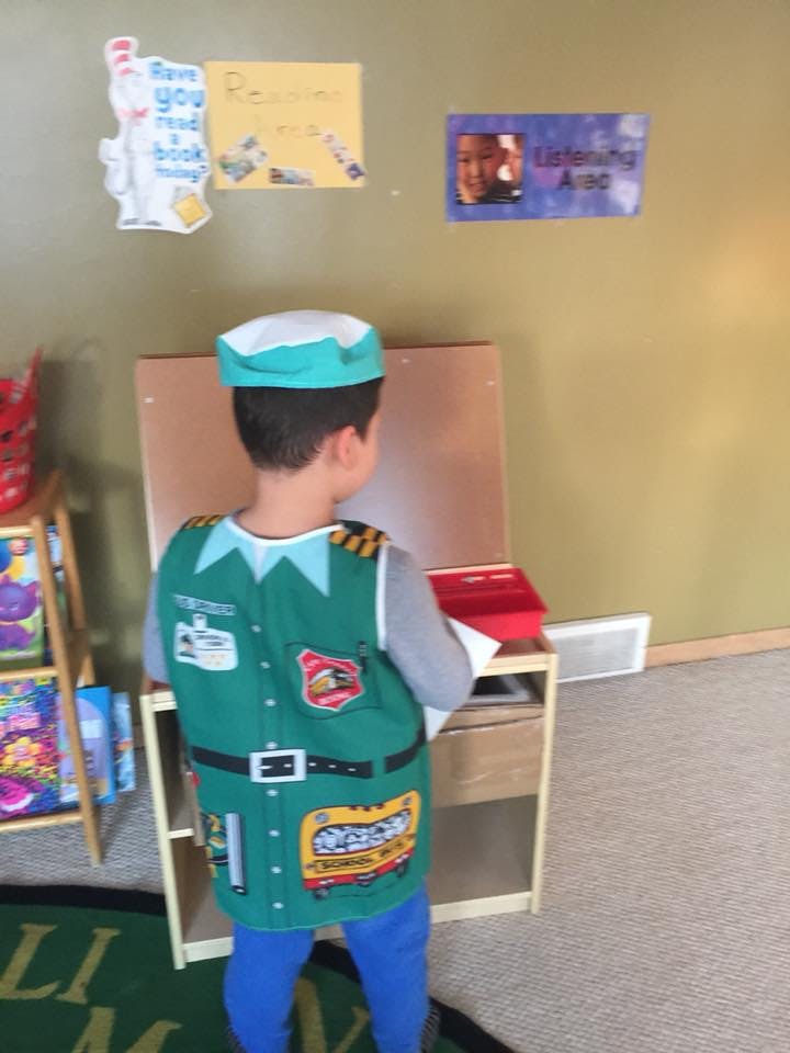 Child in a green vest and hat standing in front of an easel
