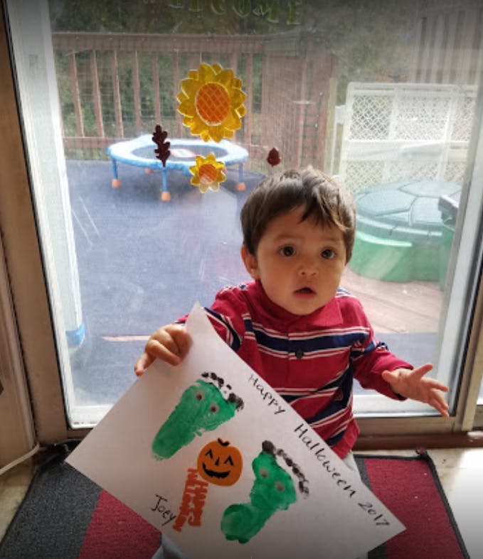 Child holding a paper with green footprint art and "Happy Halloween" text