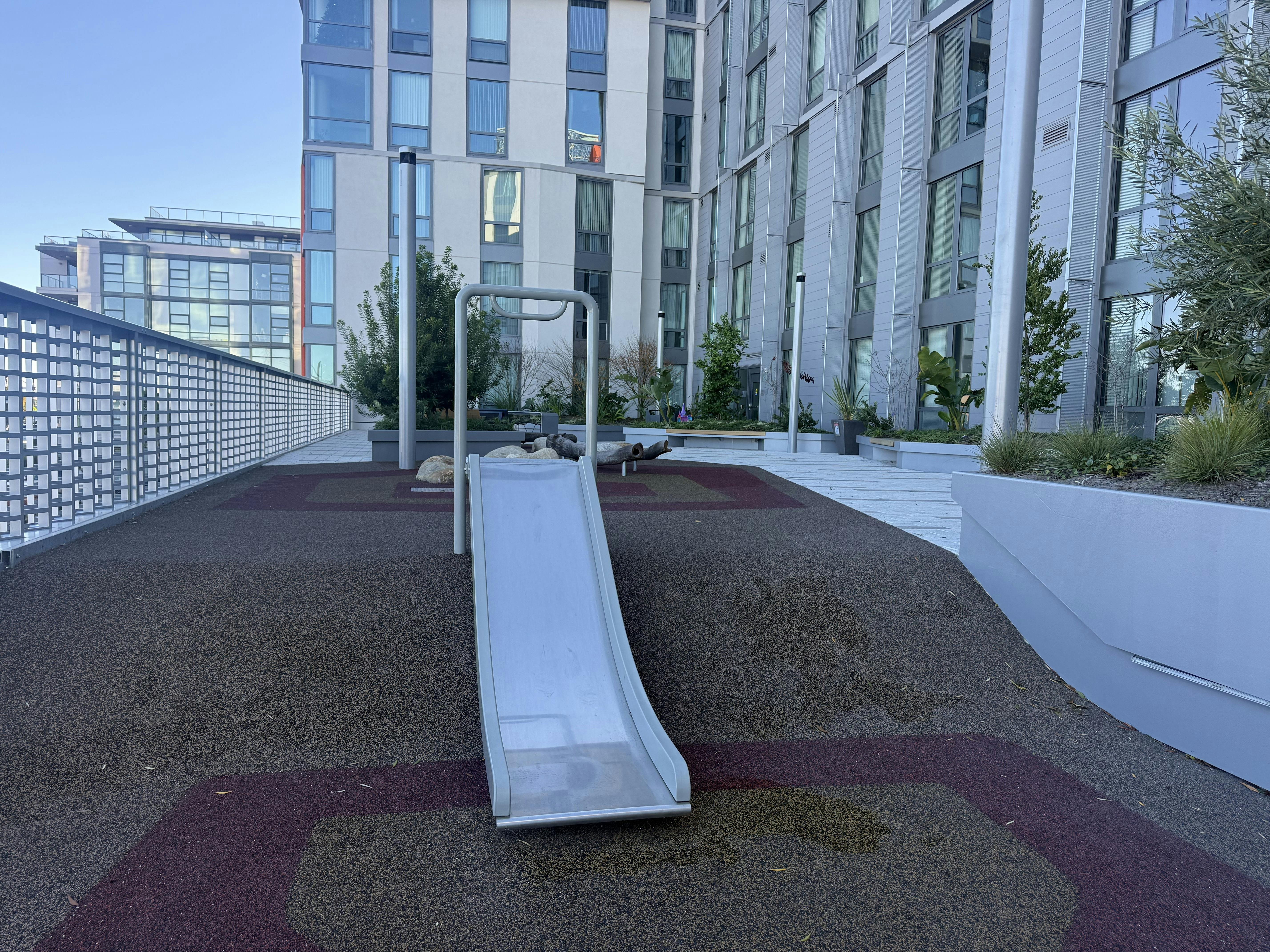 A silver slide on a rooftop playground with modern buildings in the background