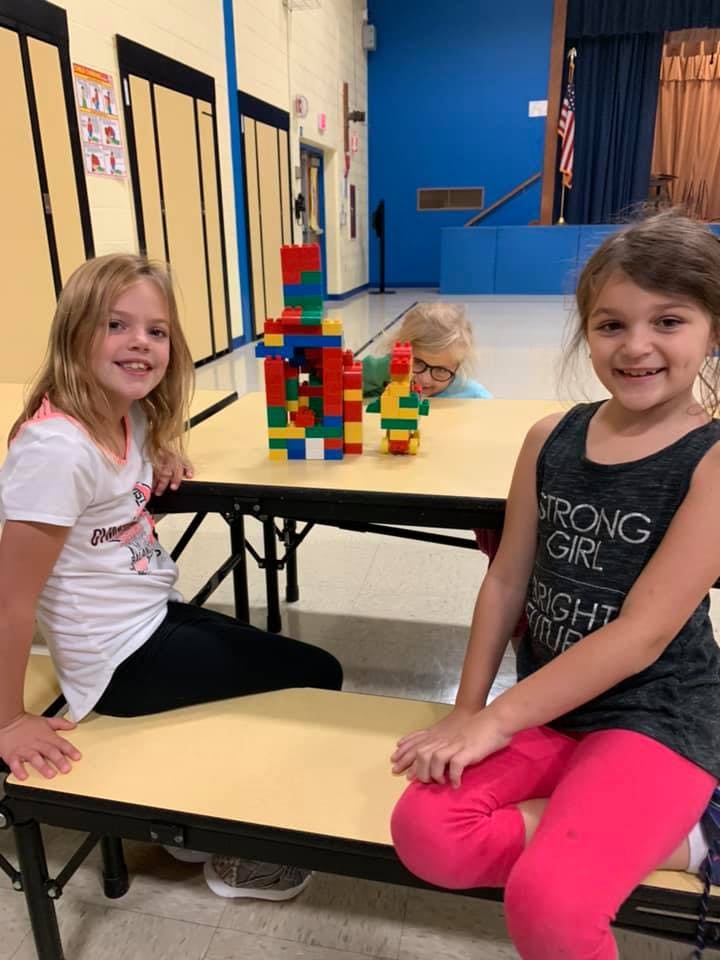 Two children sitting at a table with block creations, a third child in the background