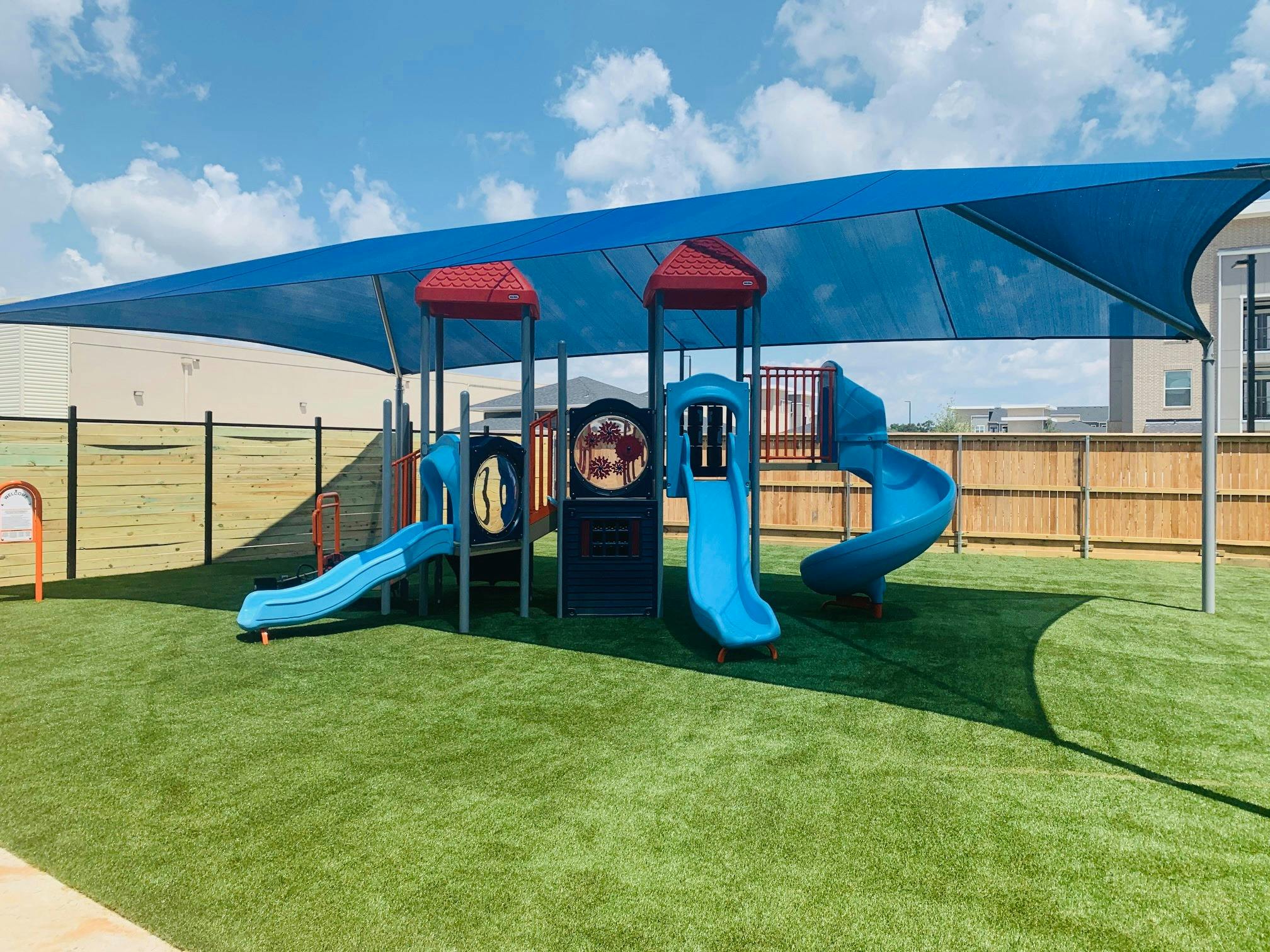 Playground with blue slides and a blue shade canopy over artificial turf