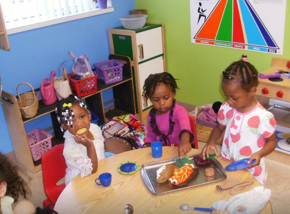 Three children playing with toy food at a table in a classroom