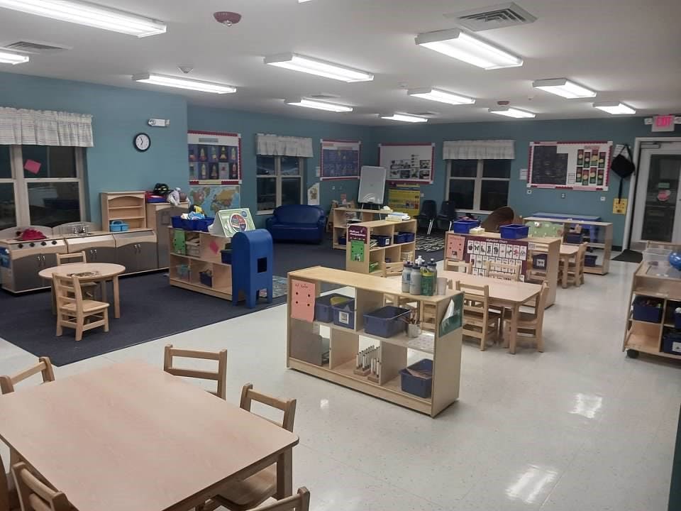 Empty classroom with small tables and chairs, play kitchen, and storage shelves