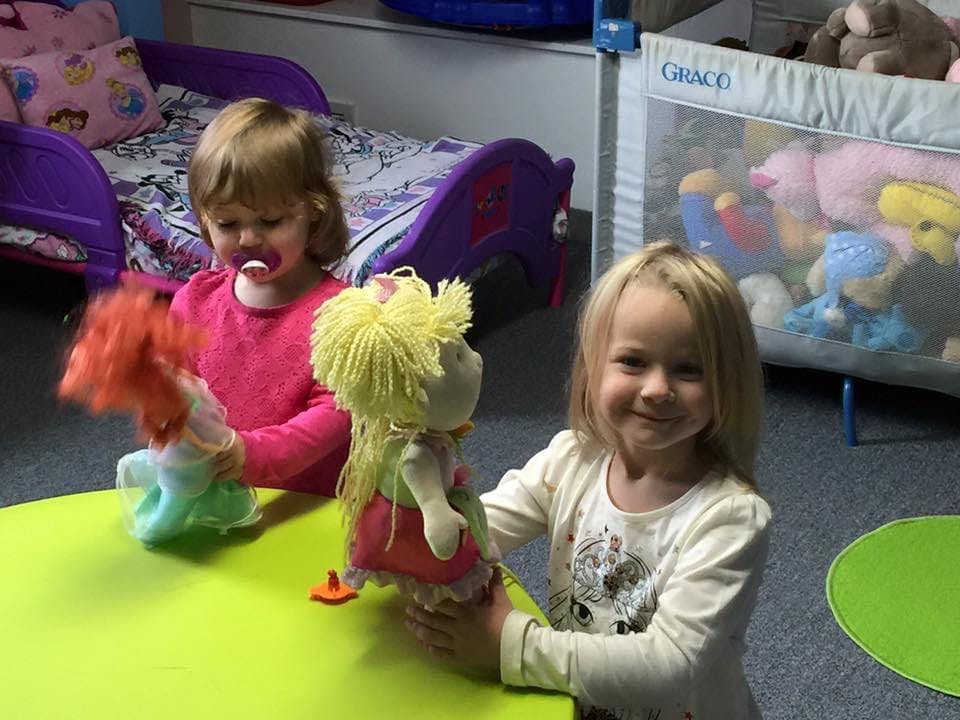 Two children playing with dolls at a table