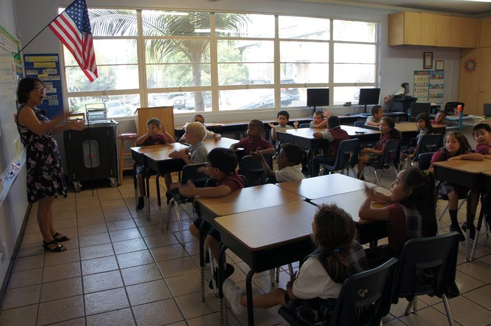 Adult speaking to children seated at desks in a classroom
