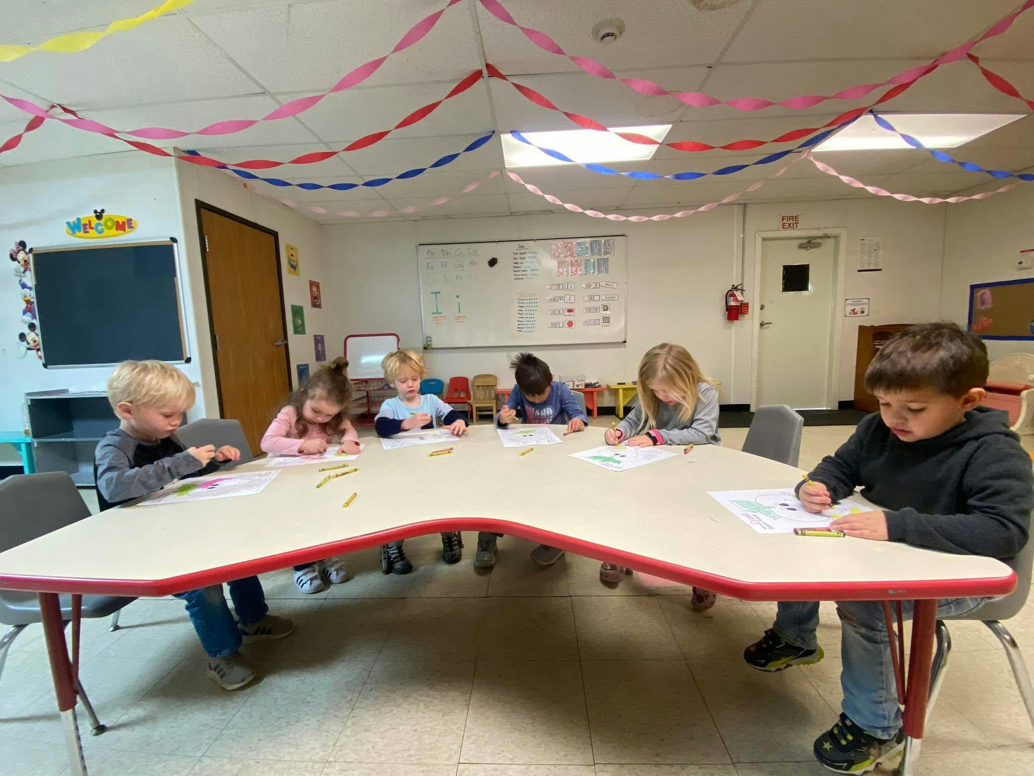 Children sitting at a table coloring in a classroom
